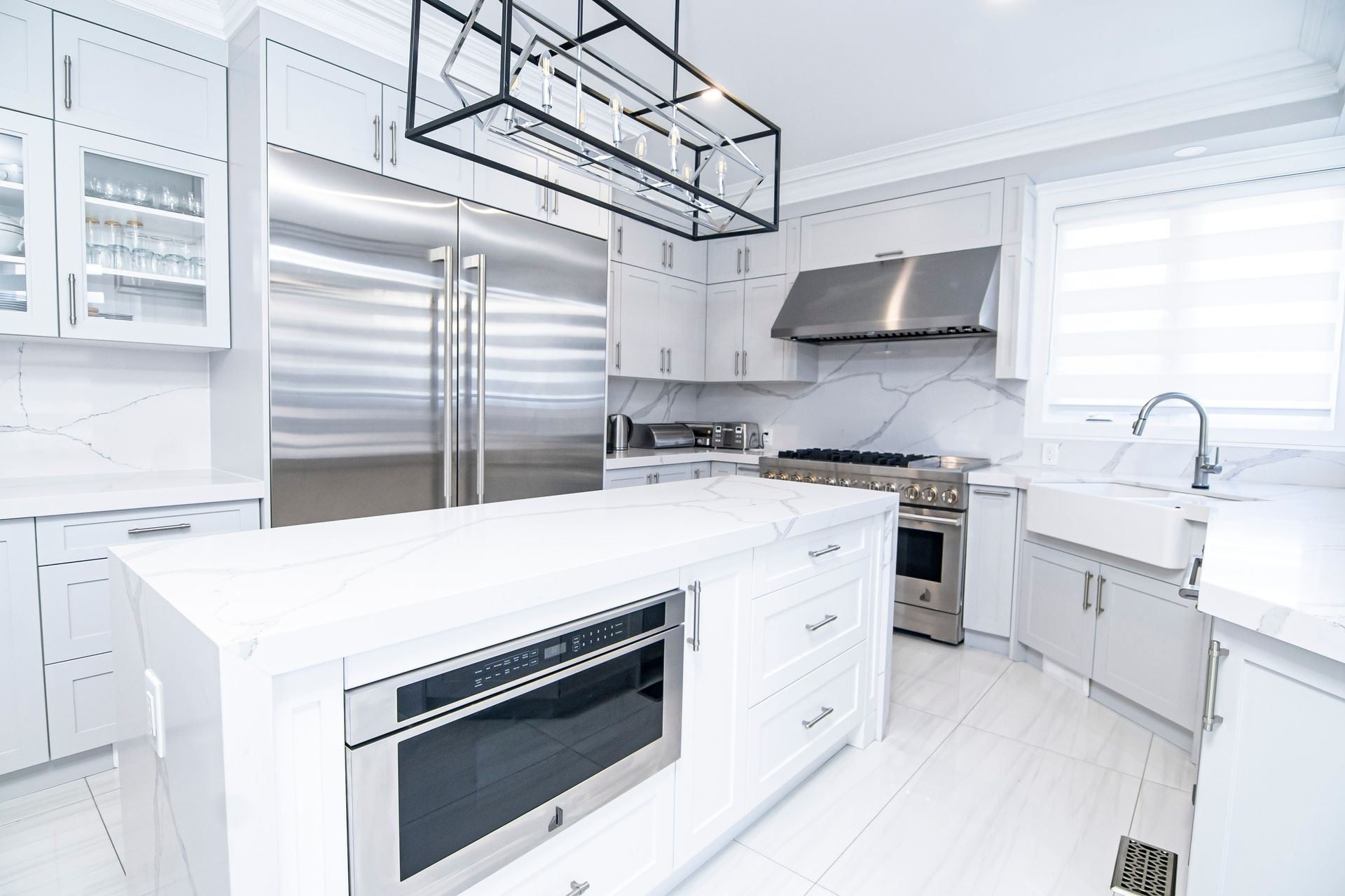 Modern white kitchen with stainless steel appliances and marble countertops.