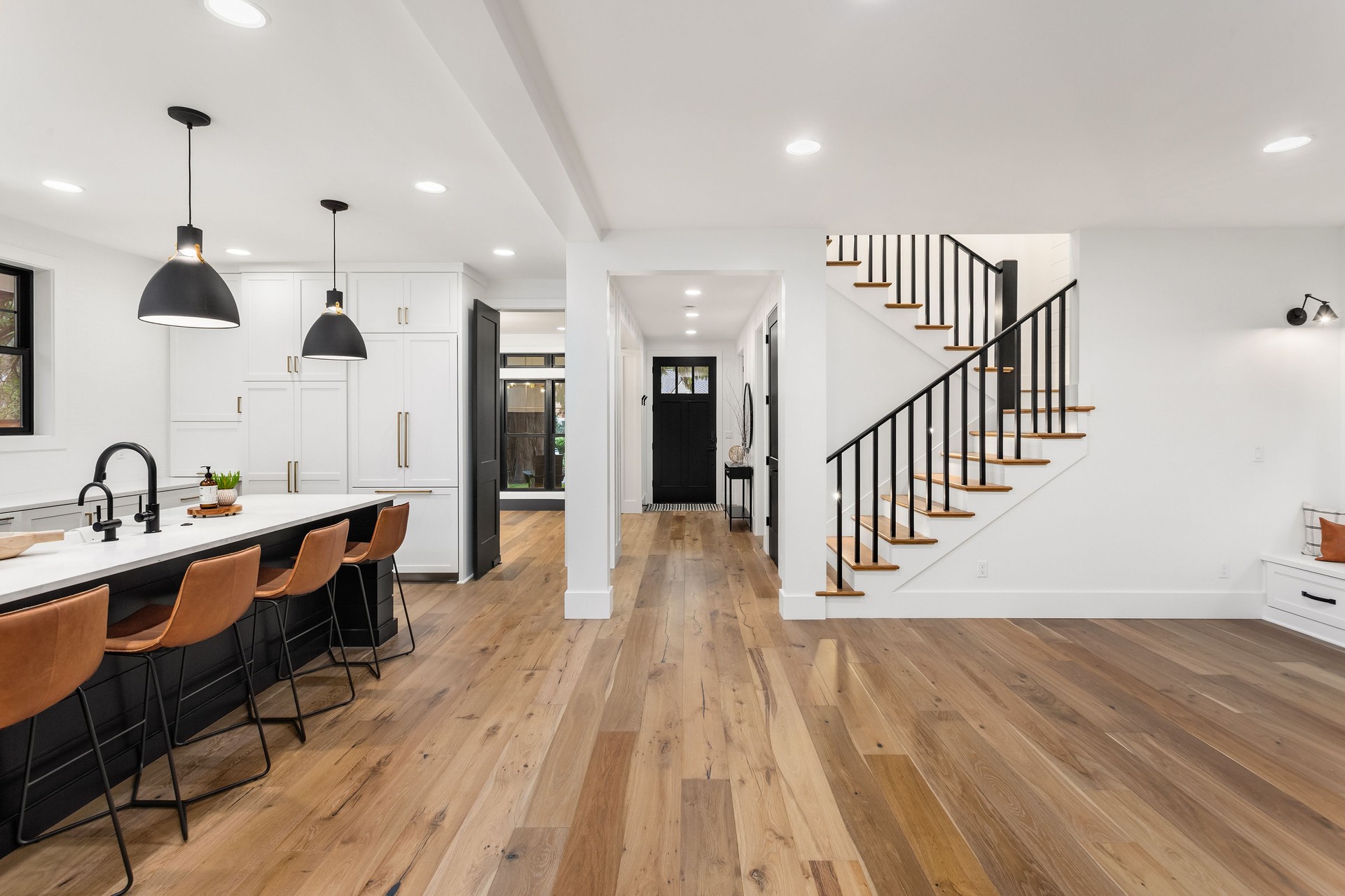 Kitchen and living room interior in new farmhouse style luxury home with open concept floor plan. Features large island with farmhouse sink, hardwood floors, and black accents.